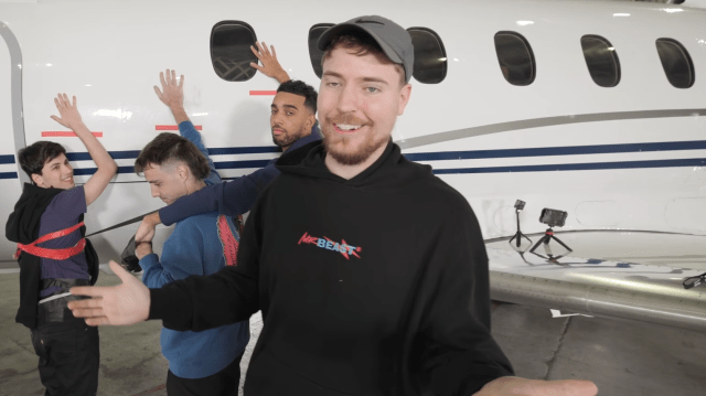MrBeast holds his hands up while standing next to a jet.