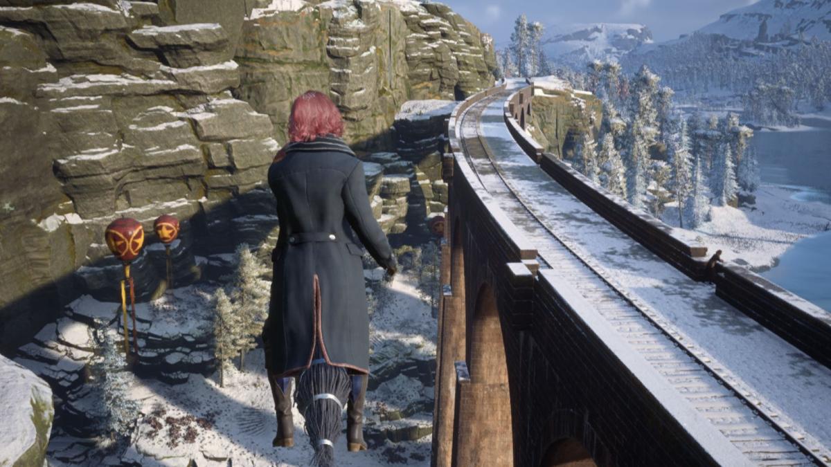 Wizard with pink hair on a broom flying over Hogsmeade station in Hogwarts Legacy.