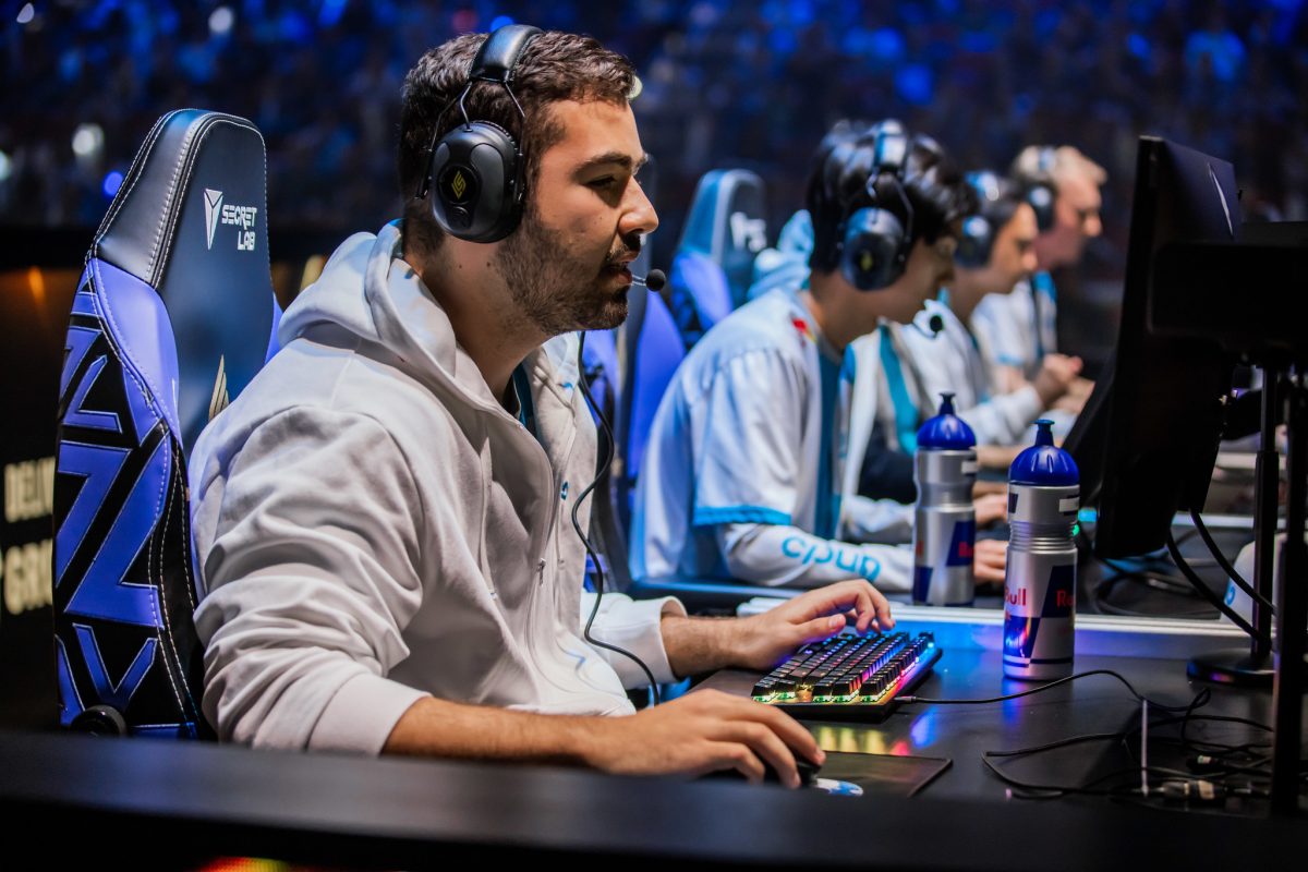 C9 Fudge sits at his PC with C9 teammates in the background.