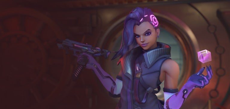 Sombra stands with her SMG and her hacking device, gesturing to an enemy in Overwatch 2.