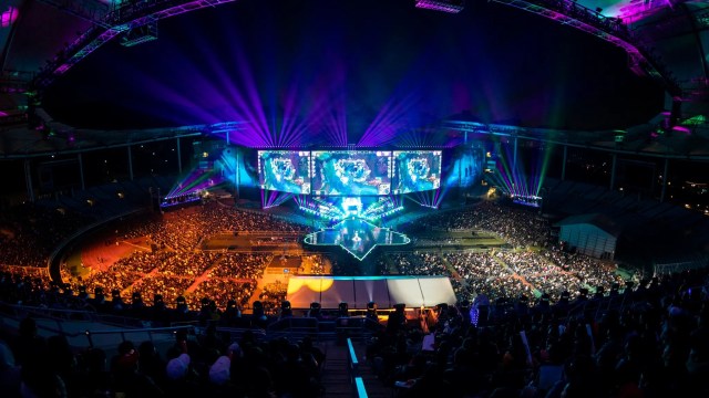 A photo of the Worlds 2018 arena. Three large screens in the middle, spectators in the foreground.