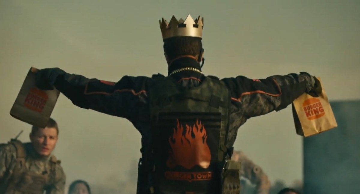 A crowned man in a Burger King outfit holding up bags of Burger King.