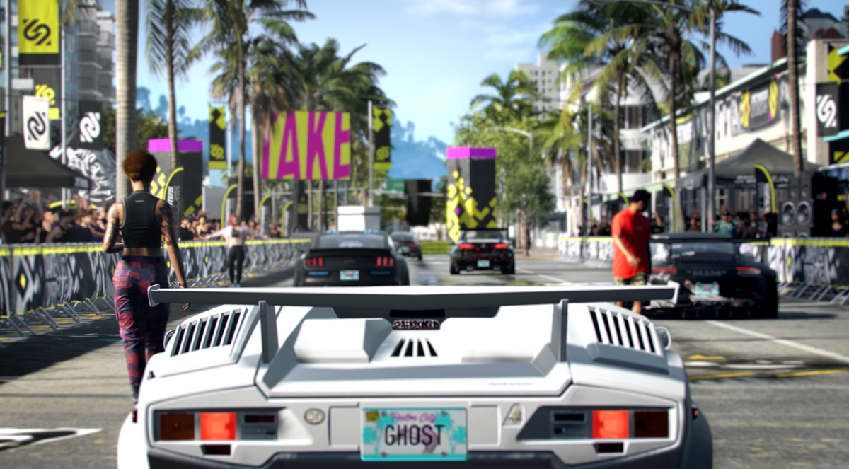 A supercar waits at the starting line of a race, with a street lined with palm trees in front of it.