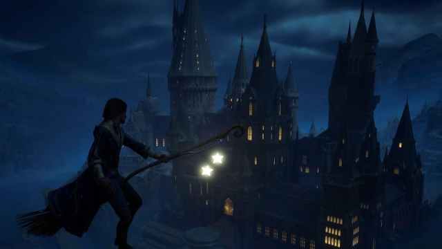 The player flying on a broom by Hogwarts at night.