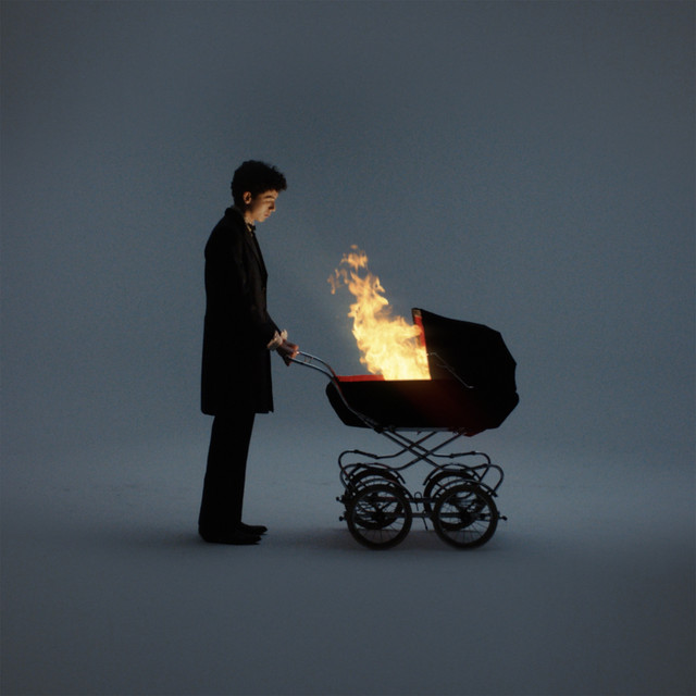 An image of the Cradles cover art from Fortnite Festival, which showcases a man looking at a burning cradle. 