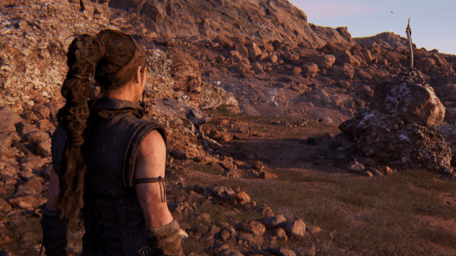 Senua looks down a path marked by a rock with a white runic symbol on it