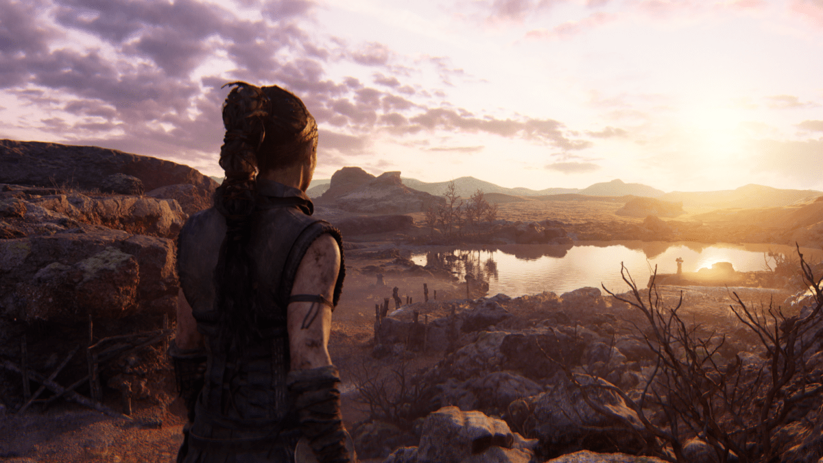 Senua looks over a lake as the sun sets in the background