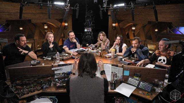The Critical Role cast sits around the table listening to Matt Mercer, who has his back to the camera