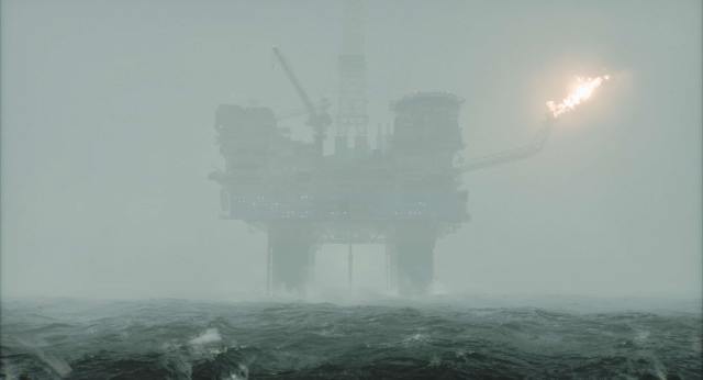 An oil rig can be seen through a layer of fog in the sea