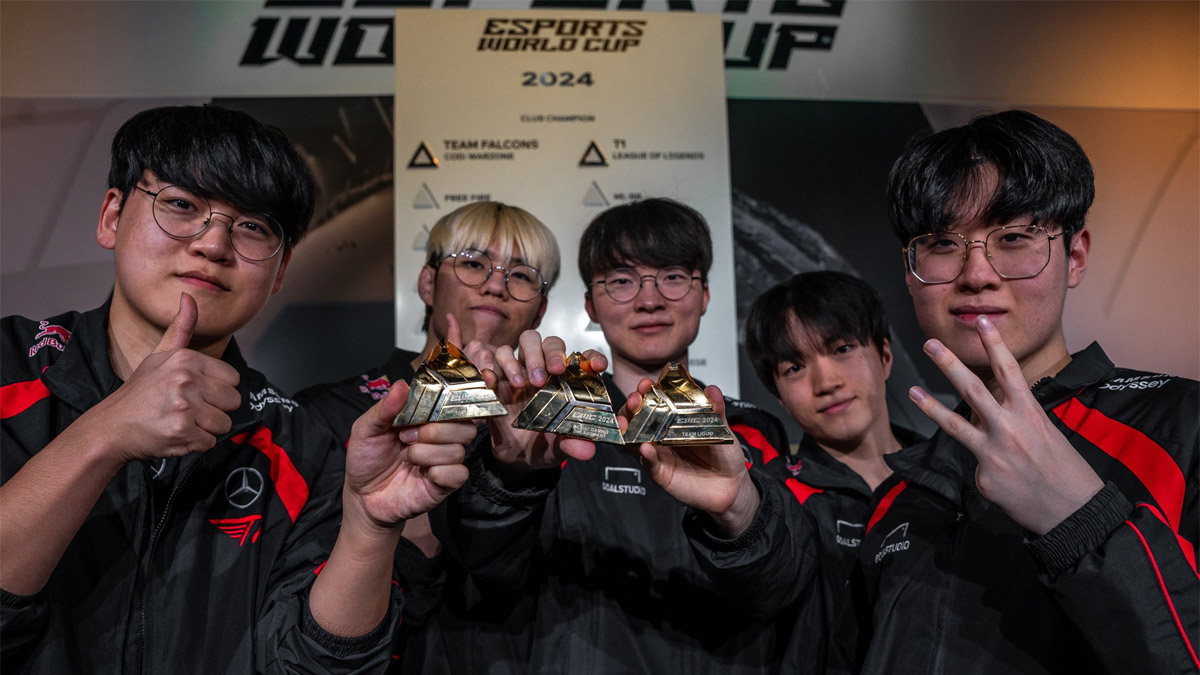 T1's LoL team stand holding the crushed trophies of their rivals at EWC.