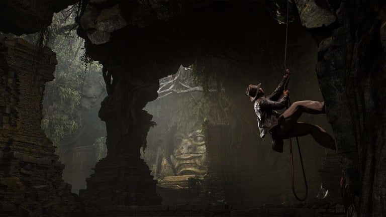 Indiana Jones climbing a rope inside a big, dark tomb with a demon statue