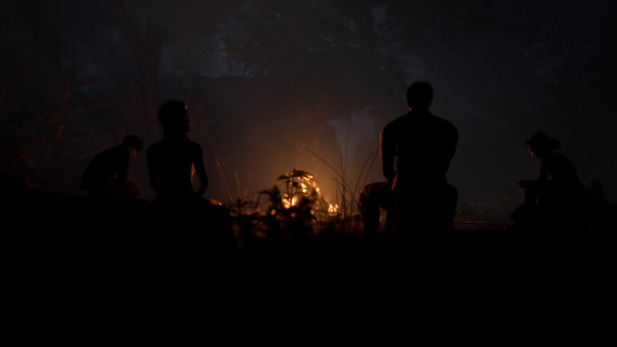 Unrecognisable characters, darkened by the night sky as they sit in front of the campfire, waiting for the trial to start