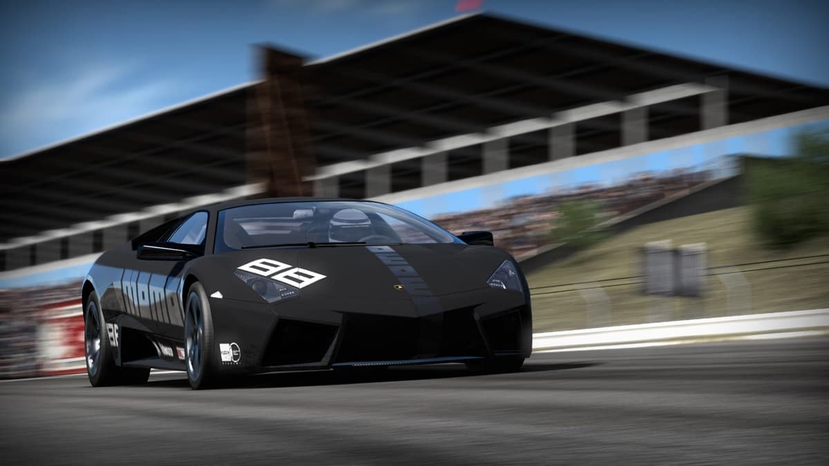 Black sports car speeding through a racetrack with crowd seats in the background