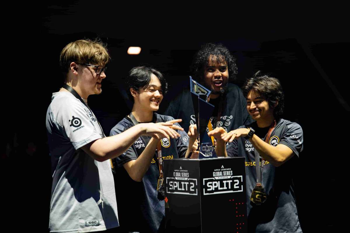 Four people surround a trophy, holding their hands out towards it