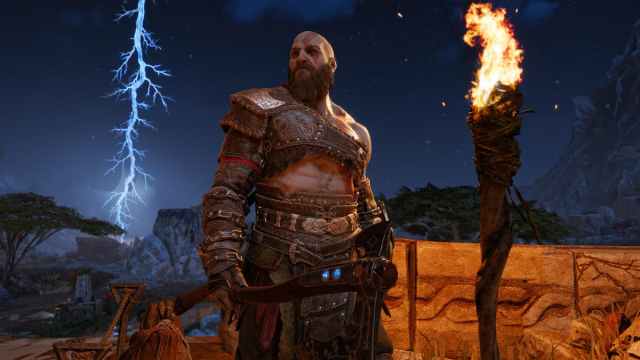 Kratos standing upright with his axe with a torch in front and a thunder strike in the far sky in background