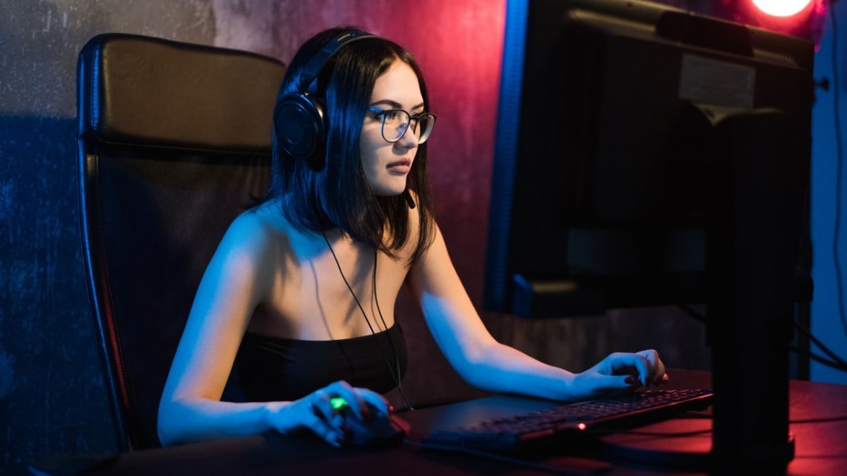 A woman wearing a headset playing a game on her computer using a mouse and keyboard