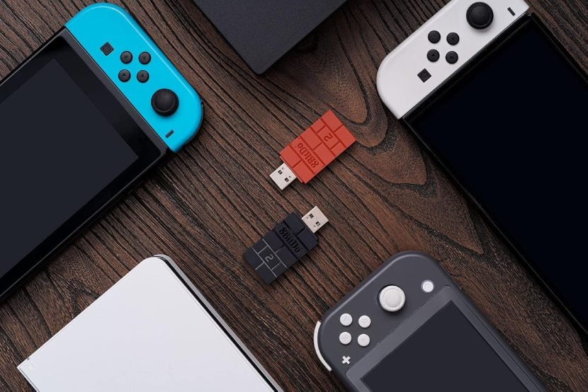 Top view of two 8bitdo Wireless Adapters, one orange and one black, surrounded by gaming devices. More details below.