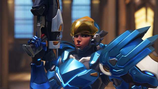 Pharah, wearing a suit of blue armor, holds up a rifle in the air.