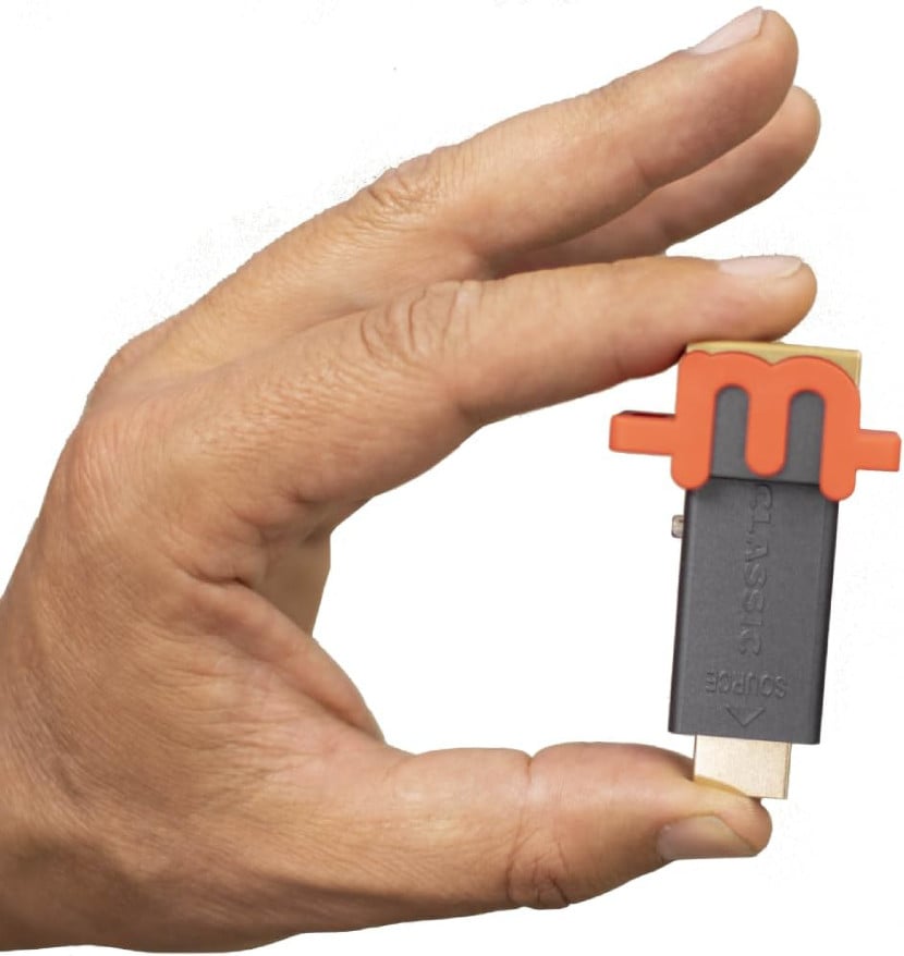 A hand holding the Marseilles mClassic between finger and thumb. The product is a USB dongle with a large lower-case M on one end. More details below.