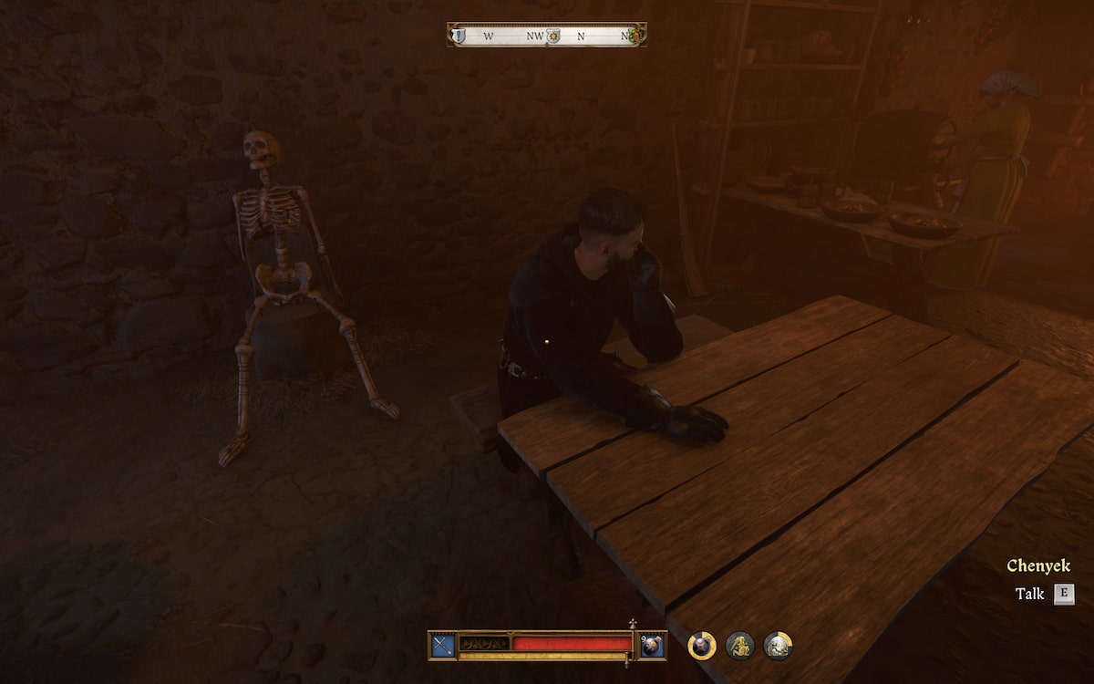 A man dressed in black sitting at a table with a skeleton propped up on a stool behind him