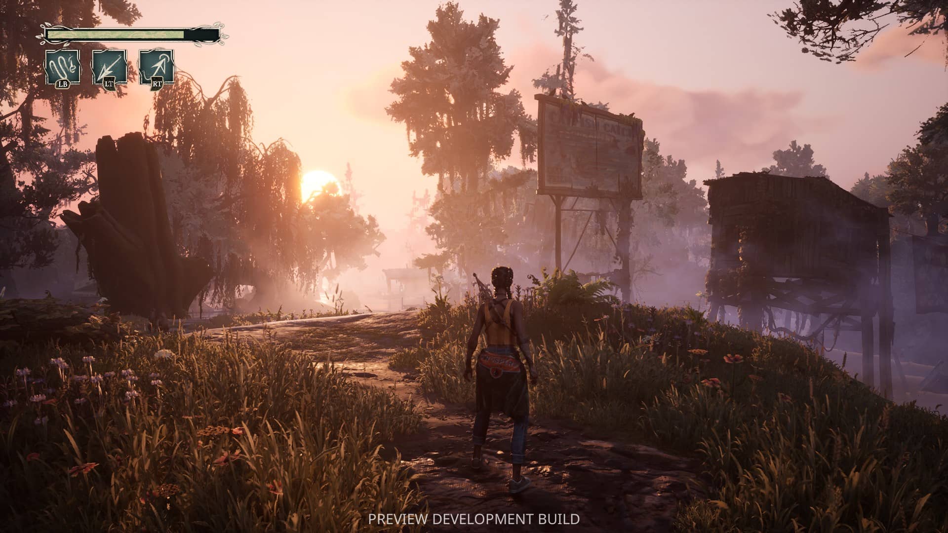 Hazel stands in a field with dilapidated buildings and a billboard, with trees and a sunset in the distance.