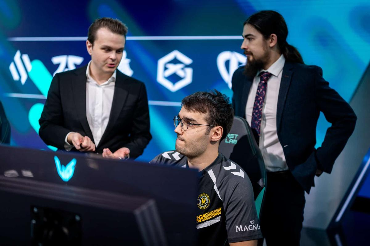 hylissang sitting in a chair onstage surrounded by his two coaches in the LEC