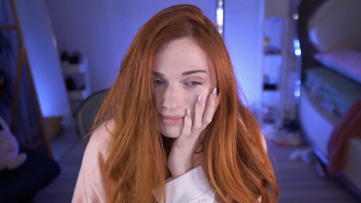 Amouranth holding her head in her left hand, looking tired